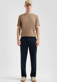 Tan korte mouwen t-shirt, donkerblauwe broek, beige sneakers en een beige pet. Eenvoudig ontwerp met een ontspannen pasvorm en geen zichtbare patronen.