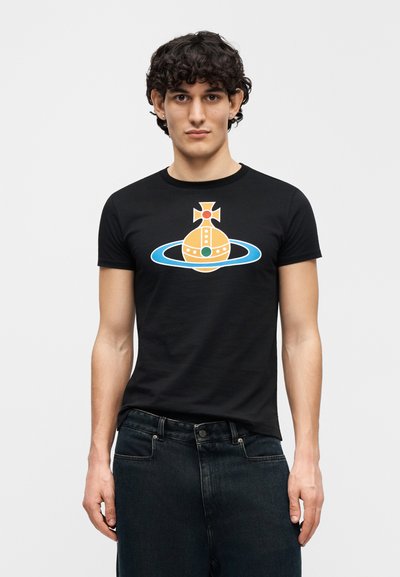 Camiseta negra de algodón con un diseño gráfico colorido de una nave espacial estilizada con un anillo azul, combinada con vaqueros oscuros.