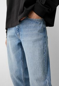 Osoba koja nosi svijetloplave traperice s rukom u prednjem džepu, u kombinaciji s crnom majicom dugih rukava.