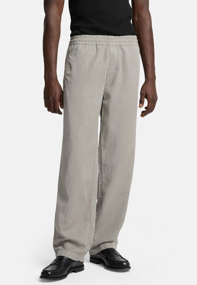 Lichtgrijze, loszittende broek met een elastische tailleband en zijzakken, gecombineerd met zwarte schoenen. Gladde stofstructuur.