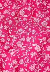 Tissu rose présentant un motif floral blanc avec diverses petites fleurs et des vignes feuillues. La texture semble lisse avec des plis subtils.