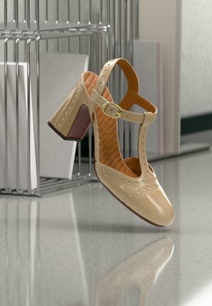 Chaussure à talon haut en cuir beige avec une bride en T, des perforations décoratives et un talon épais avec un accent bordeaux. Finition lisse.