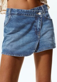 Denim suknja omotnica svijetloplave boje. Ima prednji džep, detalj s gumbom i isfrfljeni rub. Mekana tekstura s ležernim izgledom.
