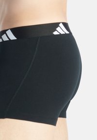 Svarta stretchboxershorts med en slät textur, som har en tjock svart midja med vit tre-strips branding framtill.