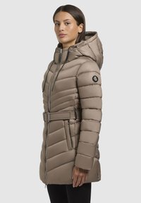 Beige pufferjas met een ceintuur in de taille, capuchon, horizontale naadpatronen, ritssluiting en een logo patch op de mouw. Smooth textuur.