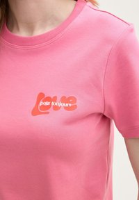 Rosa bomullströja med rund halsringning och korta ärmar, med ett "Love pour toujours"-tryck i kontrasterande röd-orange.