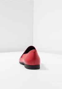 Scarpe flat rosse in pelle con punta tonda, texture liscia, suola nera bassa e design minimalista, che mette in risalto una silhouette senza cuciture.