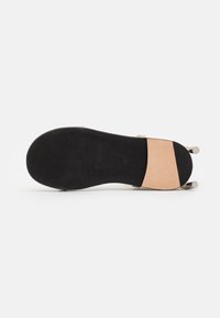 Suola di scarpa nera con un accento beige sul tallone. La texture è liscia, con una forma arrotondata e dettagli metallici sul retro.