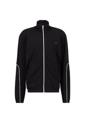 Zwarte sportjack met hoge kraag, witte ritssluiting en contrasterende witte piping langs de schouders en zakken. Glad stofgevoel.