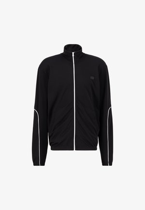 Zwarte sportjack met hoge kraag, witte ritssluiting en contrasterende witte piping langs de schouders en zakken. Glad stofgevoel.