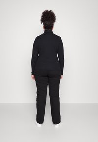 Sort langærmet top med høj krave, parret med sorte bukser og hvide sneakers. Enkel design, tætsiddende silhuet og glat tekstur.