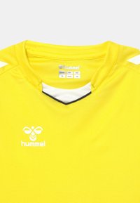 Gul sportstrøje med V-udskæring, med hvide detaljer på skuldrene og et hvidt logo på brystet. Lavet af letvægtsstof.