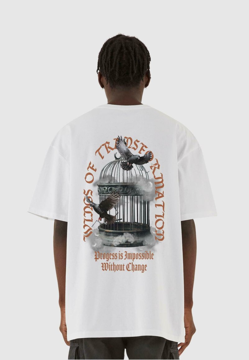 Hvid oversized t-shirt med grafik af et fuglebur, fugle i flugt og sætningen "Fremskridt er Umuligt Uden Forandring" i orange.