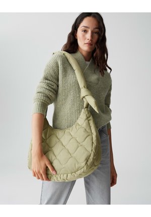 Gevoerd groene schoudertas met een zachte, gestructureerde oppervlakte en een geknoopte strap. Gekozen door een persoon in een lichtgroene trui en grijze spijkerbroek.