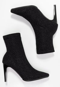 Botines negros con brillo, tacón de aguja, puntera puntiaguda y tela texturizada. Presentan un diseño ceñido similar a un calcetín para una silueta elegante.