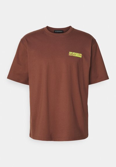 T-shirt en coton marron à manches courtes et col rond. Avec un logo graphique en texte jaune sur la partie gauche de la poitrine. Design simple.
