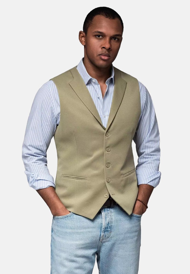 Beige strukturierte Weste über einem hellblauen gestreiften Hemd, mit einer Drei-Knopf-Front, Taschen und einem lässigen Schnitt mit hochgerollten Ärmeln.