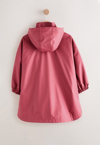 Rózsaszín vízálló dzseki kapucnival, rugalmas mandzsettákkal és laza szabással. Sima textúrájú, fa akasztón lóg egy világos háttér előtt.
