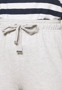 Světle šedé tepláky s elastickým pasem, s tkaničkou a stříbrnými kovovými detaily. Měkká textilie, ležérní design.