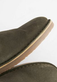 Zapato de ante en verde oliva con punta redonda, costuras claras en contraste y suela de goma marrón, con textura suave y diseño limpio.