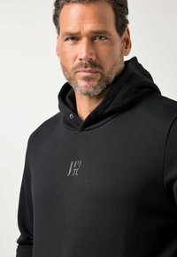 Felpa nera con cappuccio realizzata in materiale morbido, caratterizzata da un logo discreto grigio sul petto, con cappuccio con coulisse e dettagli minimalisti.