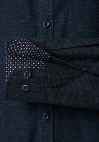 Granatowa koszula na guziki wykonana z materiału o fakturze, z kontrastową podszewką mankietów w kratę oraz ciemnymi guzikami na rękawach.