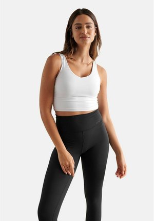 White cropped tank top paired with high-waisted black leggings. Smooth, stretchy fabric with a fitted design. Simple, solid colors.