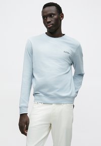 Ανοιχτό μπλε φούτερ με μακριά μανίκια, στρογγυλή λαιμόκοψη και ριμπ μανσέτες. Διαθέτει μικρό σκούρο λογότυπο στο στήθος. Μαλακή υφή υφάσματος.