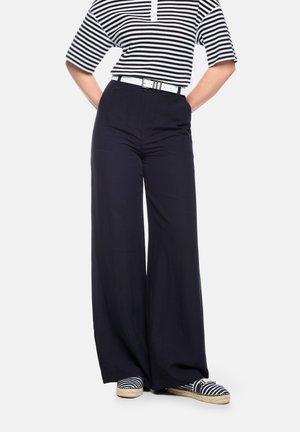 Person wearing black wide-leg pants, white belt, black and white striped short-sleeve top, and matching striped espadrilles, hands on hips.