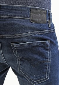 Jeans de mezclilla en un lavado oscuro con un acabado texturizado. Presenta acentos de costura, una etiqueta de cuero con la marca y dos bolsillos traseros.