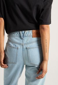 Jeans in denim azzurro chiaro con vita alta, dotati di una toppa in pelle marrone testurizzata sul retro e distinti taschini posteriori.