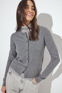 Grijze gebreide cardigan met een ronde halslijn, sluiting met knopen aan de voorkant en lange mouwen. Glad textuur en aangesloten ontwerp. Draagster combineert met lichtgrijze jeans.
