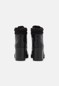 Botines de cuero negro con un puño de forro polar negro doblado y un tacón de plataforma texturizado. Acabado suave con costuras detalladas en los lados.