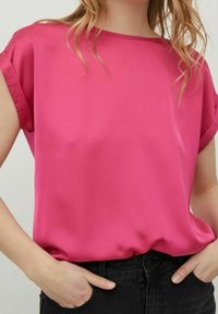 Blusa in raso fucsia a maniche corte con vestibilità rilassata, texture morbida e scollatura a girocollo, abbinata a pantaloni neri a vita alta.