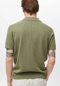 Polo majica kratkih rukava u maslinasto zelenoj boji, sa rebrastom teksturom i vertikalnim prugama. S ovratnikom i prilagođenim strukom.