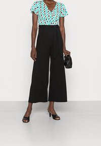 Černé kalhoty s širokými nohavicemi a přizpůsobeným pasem, kombinované s multicolorovou blůzou se vzorem vln a výstřihem do V a krátkými rukávy.
