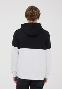 Felpa con cappuccio caratterizzata da una parte superiore nera e una parte inferiore bianca, con polsini e orlo a costine, realizzata in un tessuto morbido.