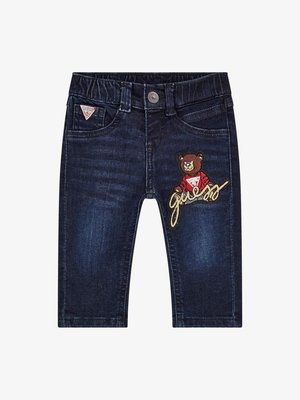 Jeans de mezclilla azul oscuro con un acabado texturizado, que presentan un oso bordado con un suéter rojo y el logotipo de "Guess". Diseño clásico de cinco bolsillos.