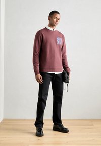 Felpa bordeaux con stampa grafica blu, camicia bianca sotto, jeans neri e scarpe nere. Texture liscia e design casual.
