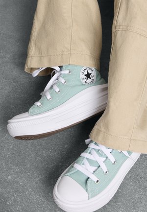 Zapatillas Converse de lona verde claro con suelas y cordones de goma blanca. Presentan un parche de logo redondo en el lado exterior y una puntera plana y ancha.