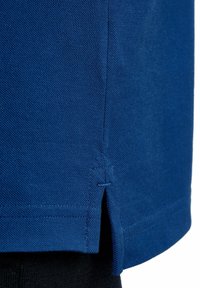 Niebieska koszulka T-shirt z fakturowanego materiału, z boku rozcięciem na dolnym brzegu i wzmocnionymi szwami. Czarny materiał widoczny pod spodem.