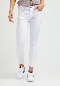 Bílé skinny džíny z hladké bavlněné směsi, s designem pěti kapes, zipovým zapínáním a decentním prošíváním, doplněné bílými teniskami.