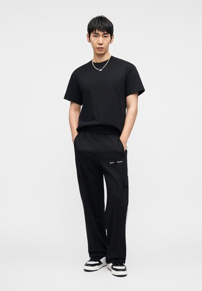 Μαύρο κοντομάνικο μπλουζάκι συνδυασμένο με μαύρο cargo παντελόνι με πλαϊνές τσέπες και κεντημένο κείμενο. Ολοκληρώνεται με μαύρα και λευκά αθλητικά παπούτσια.