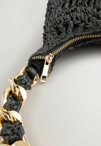 Gewebte schwarze Tasche mit strukturierter Oberfläche, ausgestattet mit einem goldenen Reißverschluss und akzentuierten kräftigen goldenen Kettenriemen. Nahaufnahme des Reißverschlussdetails.