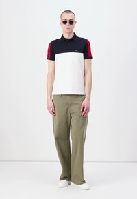 Pique-skjorte i marineblå, hvit og rød fargeblokkdesign; korte ermer; lett stoff; kombinert med olivengrønne vide bukser og hvite sko.