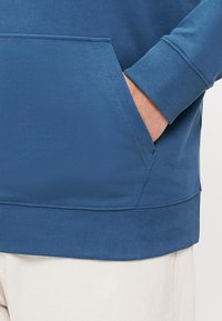 Felpa blu con una grande tasca frontale, polsini e orlo a coste. Tessuto morbido, design senza cuciture, adatta per un abbigliamento casual.