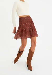 Falda de longitud a la rodilla con estampado floral en color óxido, con un diseño de volantes en capas, hecha de tela ligera. Combinada con botas de tacón de ante marrones.