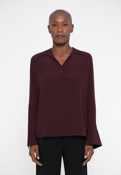 Burgundy lightweight blouse with a collar, long bell sleeves, smooth texture, and a relaxed fit, paired with black trousers.