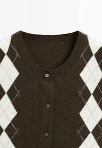 Brown cardigan featuring an argyle pattern with white diamonds. Soft texture, ribbed collar, and three round buttons at the front.