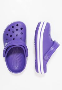 Zoccoli viola con fori di ventilazione, cinturino posteriore e una striscia bianca lungo la suola. Realizzati in materiale leggero e flessibile.